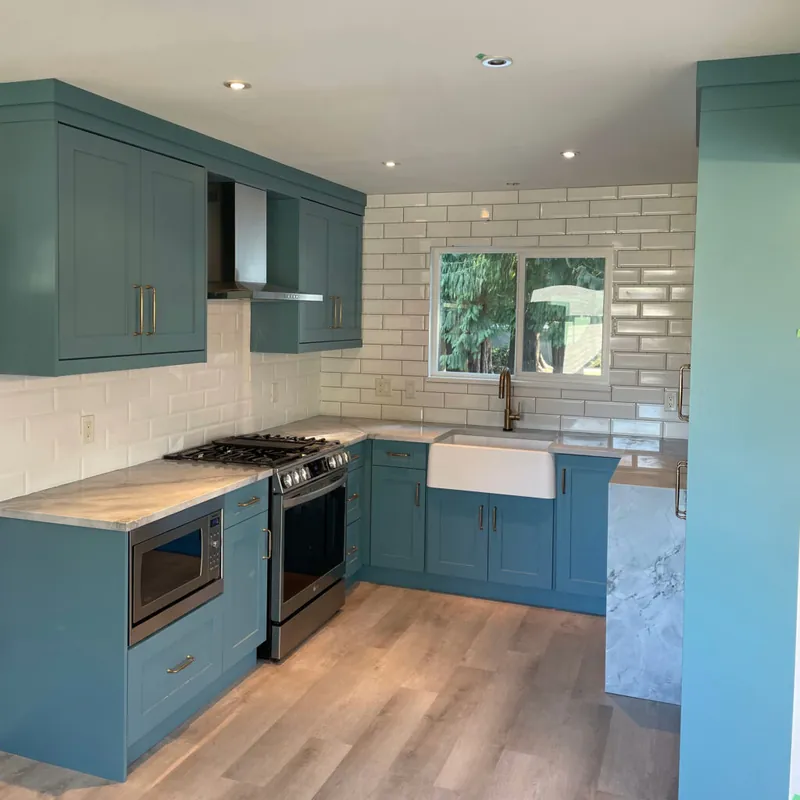 A renovated kitchen in deep teal cabinetry with a white brick backsplash and a farmhouse sink.