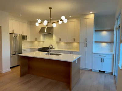 A finished white kitchen with a large island and stone counters, in a house taken back to the studs.