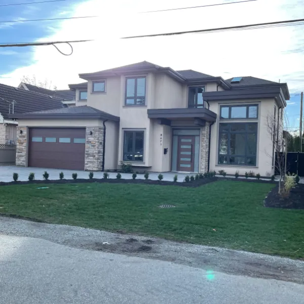 A large two-storey custom home with a stone base, dark trim and a wide paved forecourt.