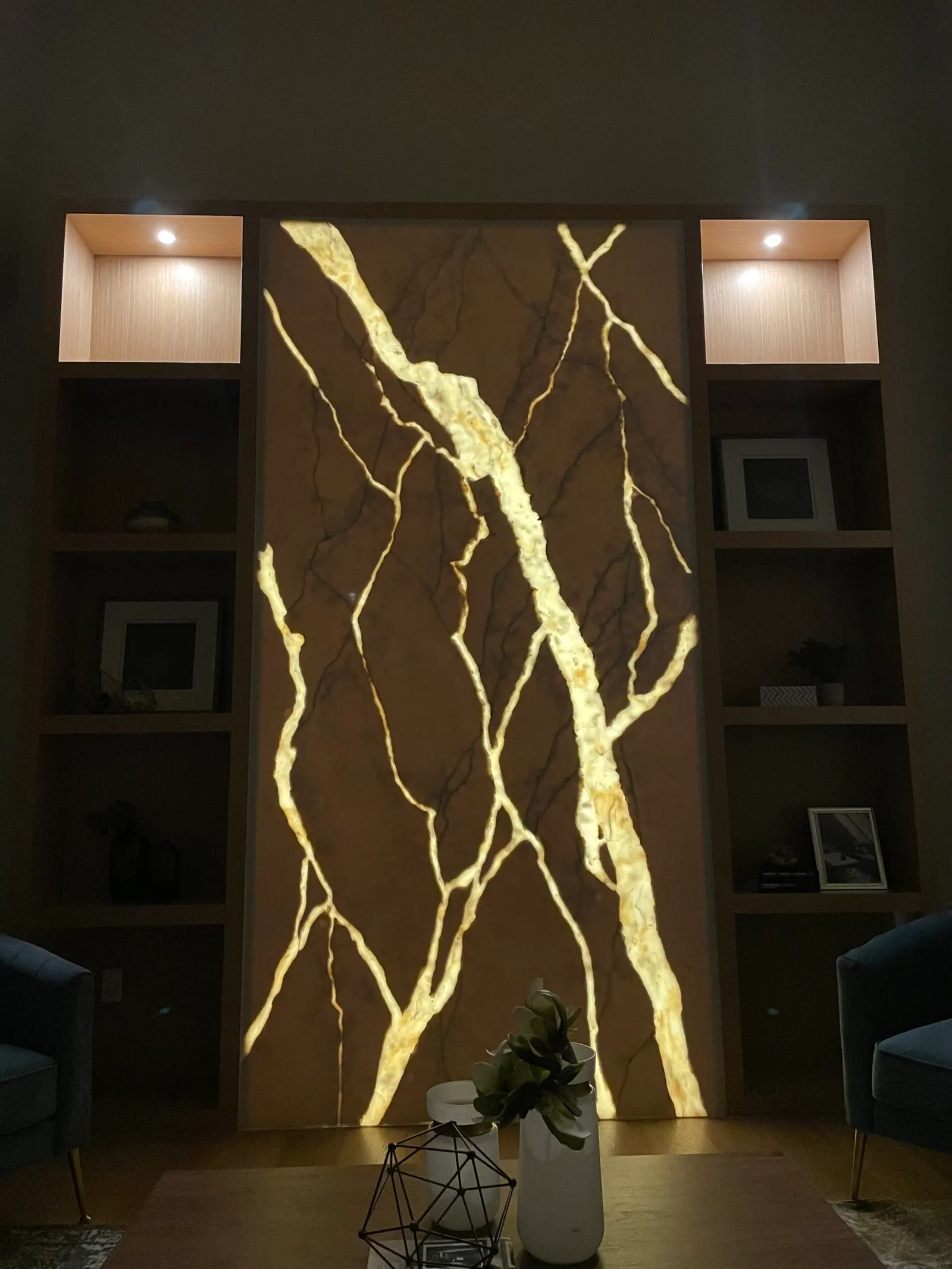 A backlit stone feature wall glowing between built-in shelving in a finished living space.