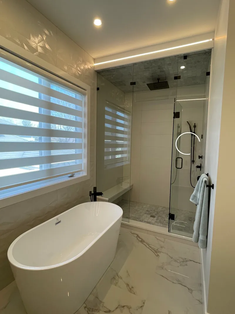 An ensuite with a freestanding tub under a window, beside a frameless glass shower in large-format tile.