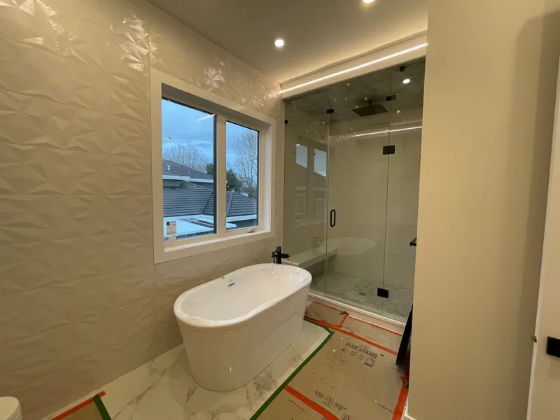 An ensuite with a sculpted textured feature wall, a freestanding tub, and the floor still protected.