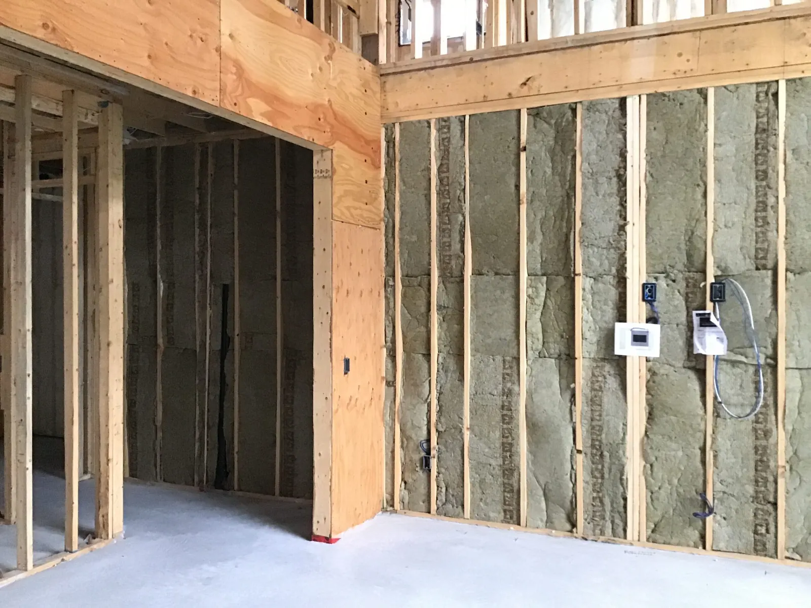 A framed interior at rough-in, insulation batts in the wall bays and boxes wired, on a broom-clean slab.