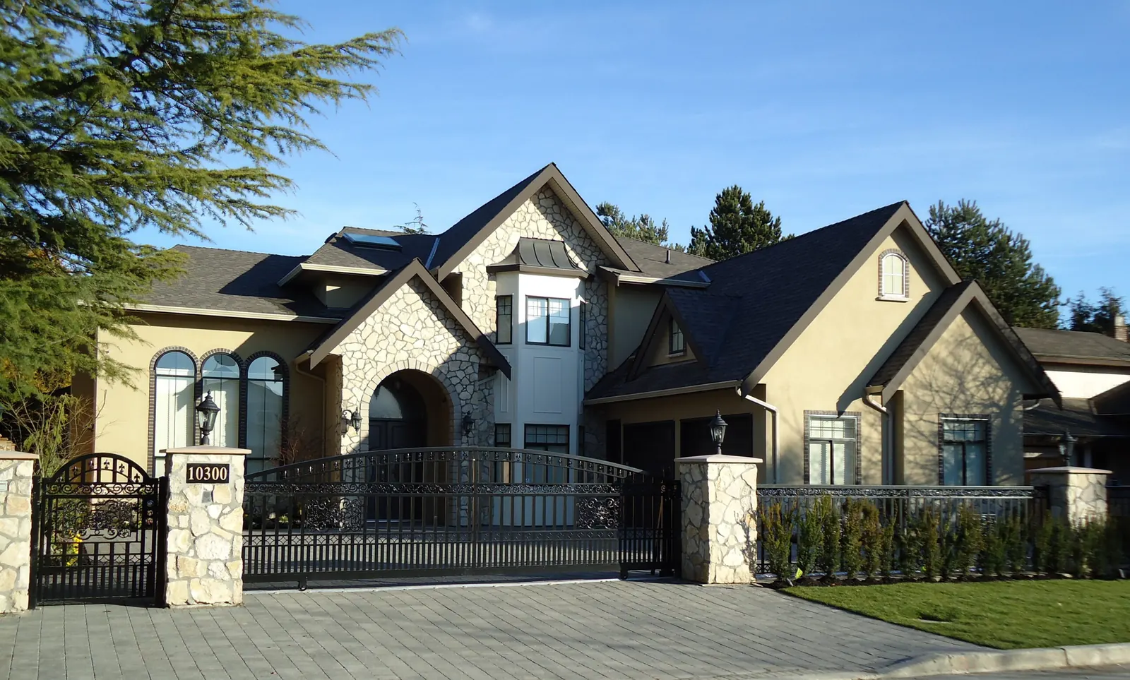 A large stone and stucco custom home behind its own gates, the full front elevation and both gables in one frame.