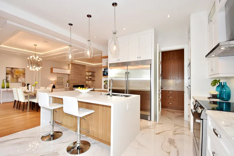 A white kitchen in marble-look stone with a wood-panelled island, pendant lighting and a dining room beyond.