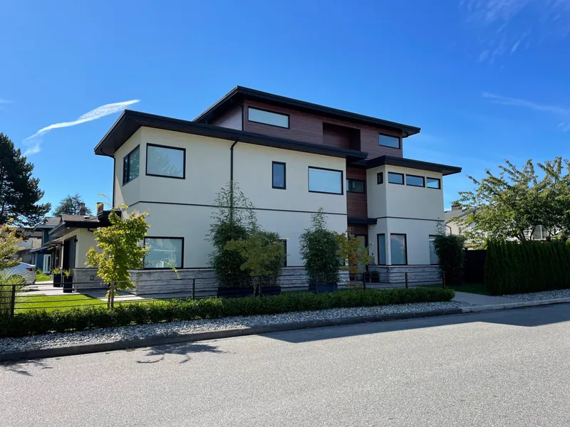 A modern three-storey custom home with a flat roof and rendered walls, seen from across the street.
