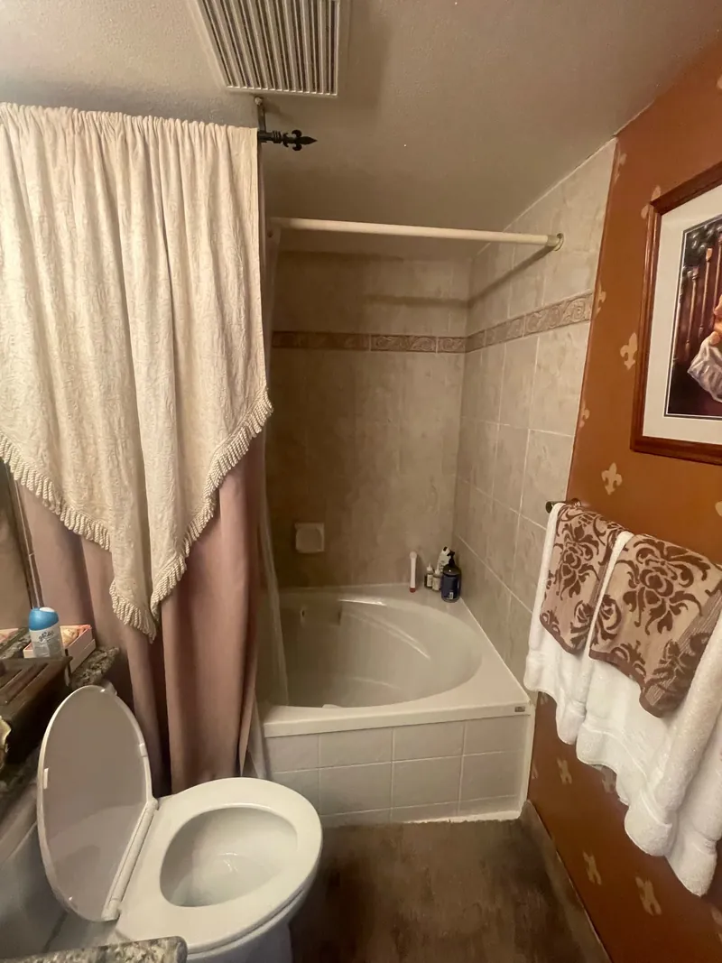 Before — A renovated bathroom in marble-look tile with a curbless walk-in shower, grab bars and a fold-down teak bench.