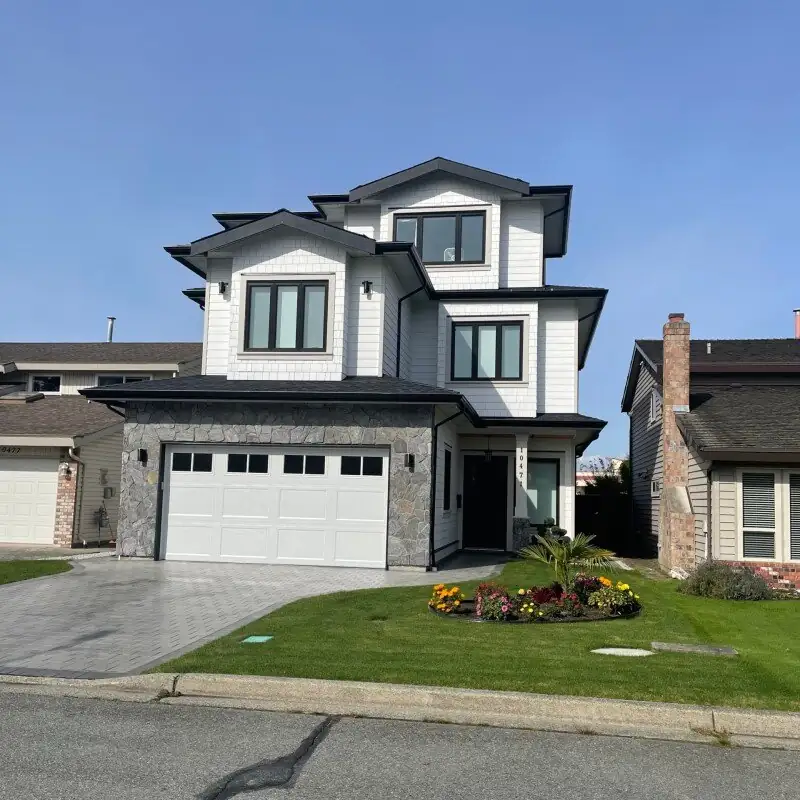 A finished custom home in daylight — white shingled gables, a dark roofline and a stone-faced double garage.