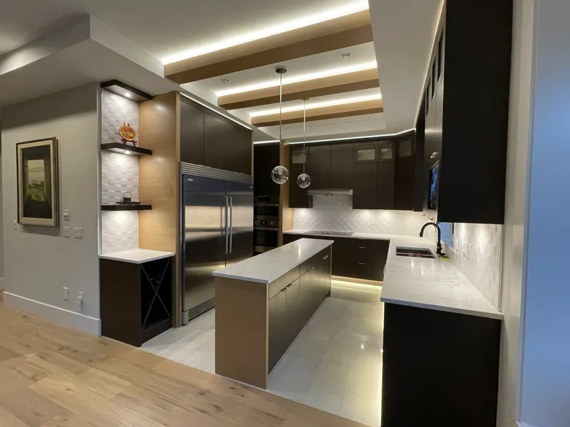 A dark lacquered kitchen with an integrated hood, stone counters and lit display niches.